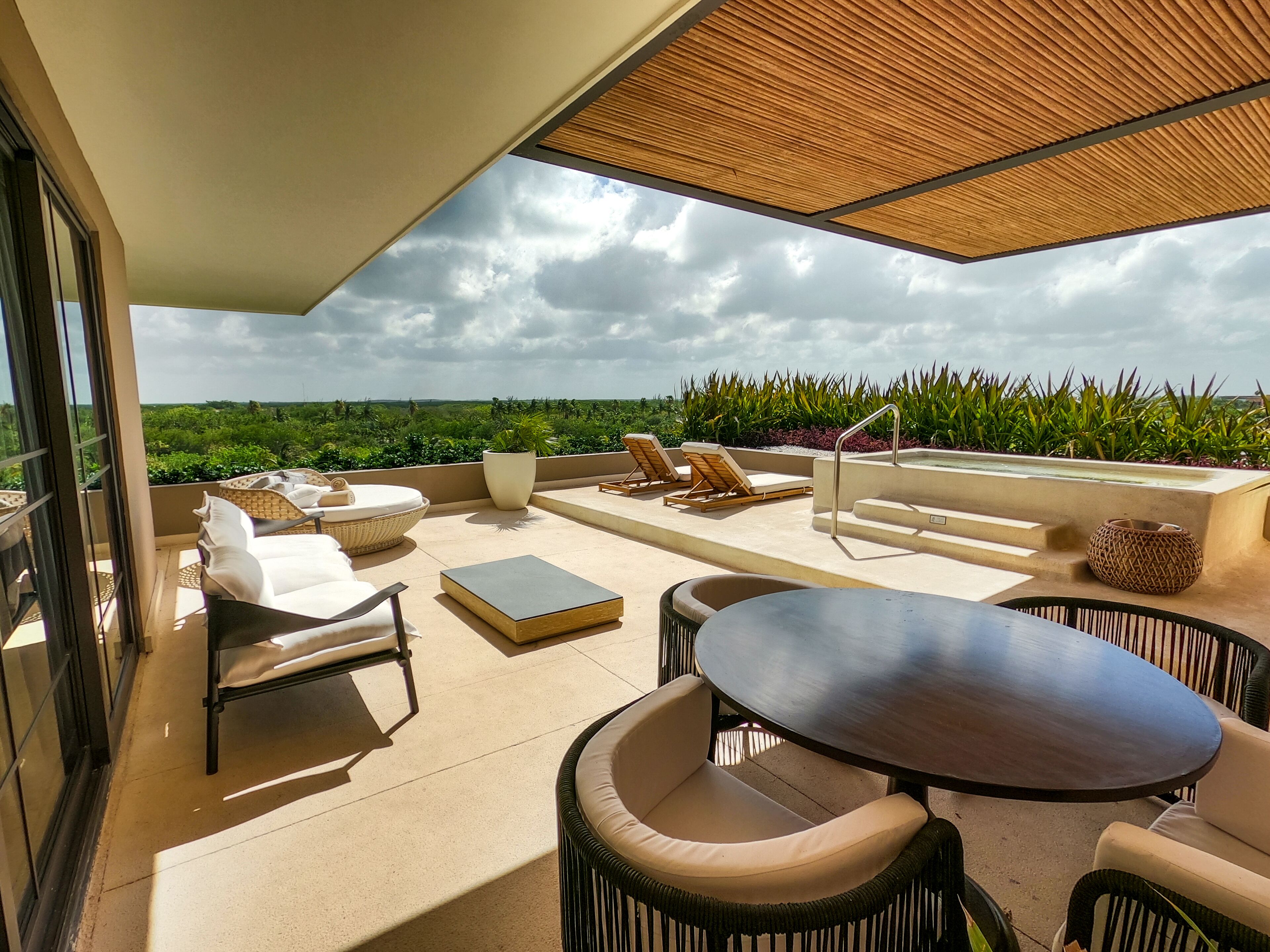 A rooftop terrace with a pool, lounge chairs, a table, and a view of the landscape.