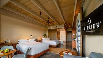 Een hotelkamer met twee bedden, een bureau met fruit, een stoel, een bank en een plafondventilator.