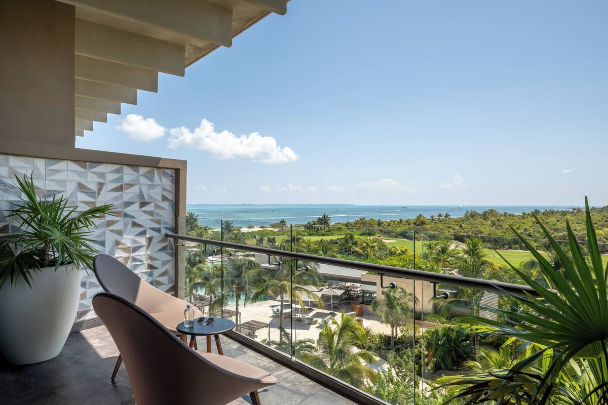 A balcony with a view of the ocean, a potted plant, and a modern chair.