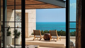 Un balcon avec deux chaises en bois et un grand pot de fleurs, donnant sur une mer d’un bleu limpide.