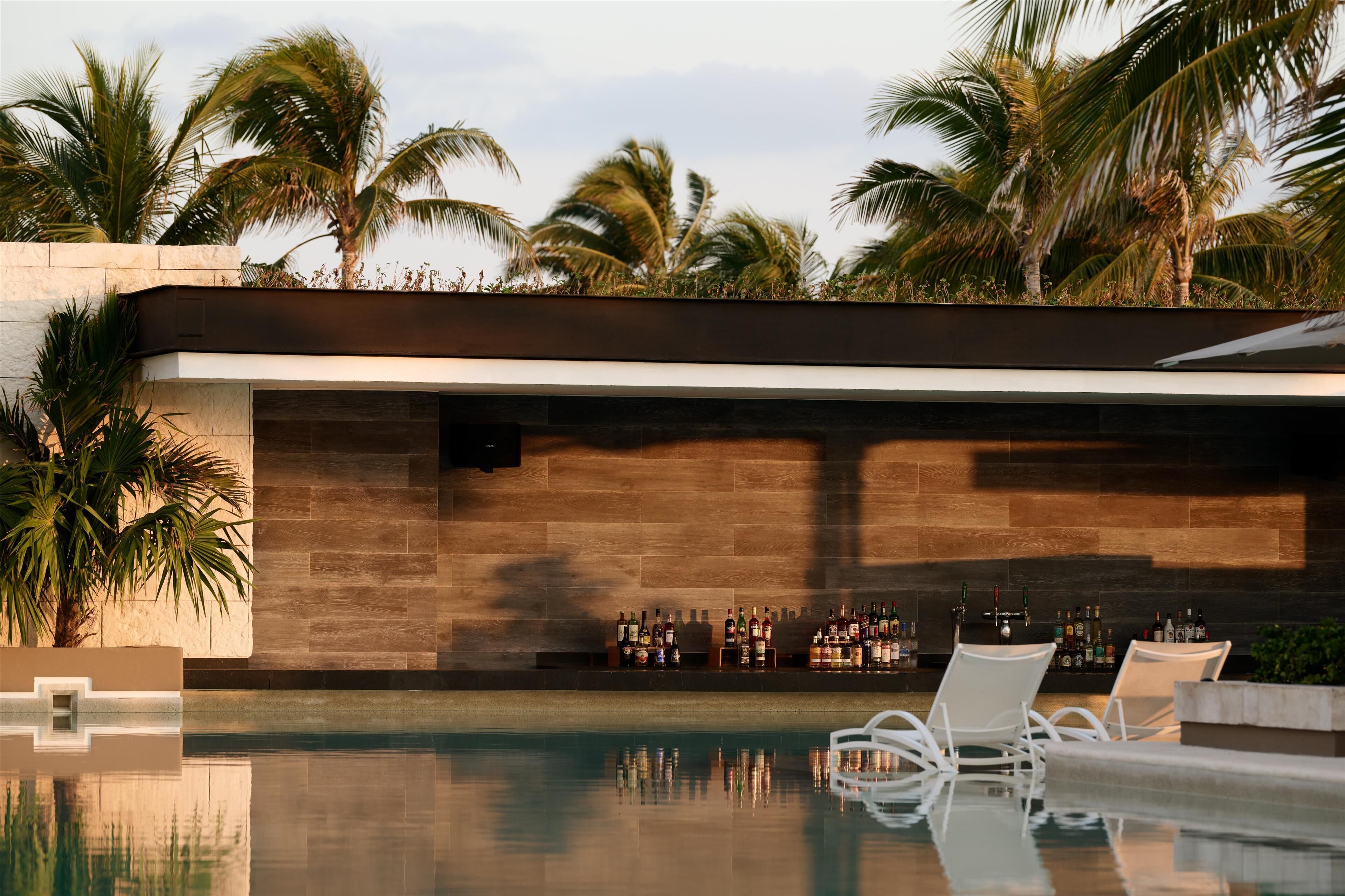 A pool area with lounge chairs, a bar with various bottles, and palm trees in the background.