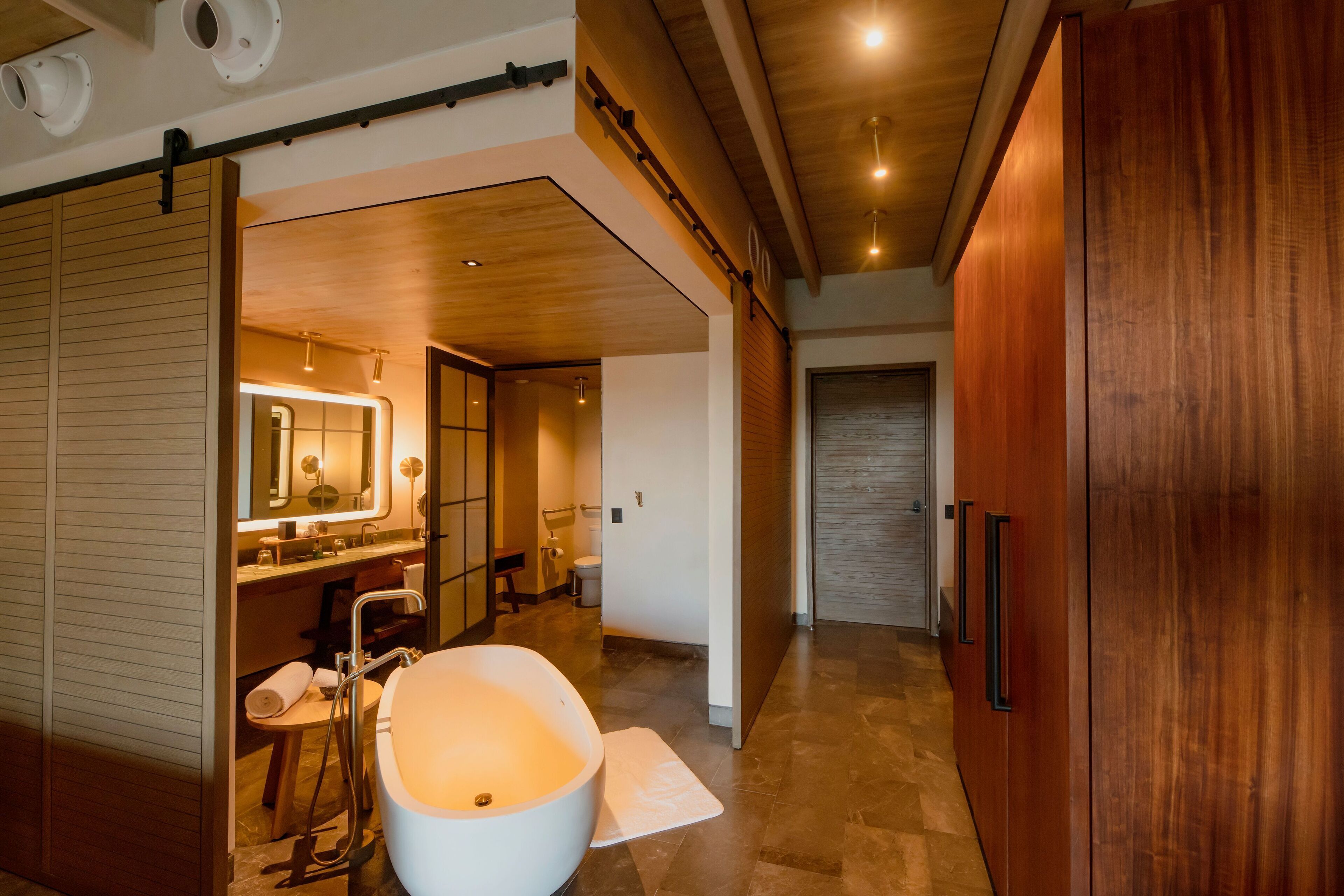 A modern bathroom with a large bathtub, a vanity with a mirror, and a wooden door.
