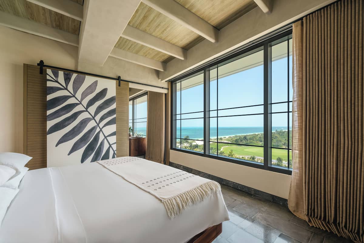A bedroom with a large window, a bed, and a view of the ocean.