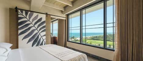 Un dormitorio con un ventanal grande, una cama y vista al océano.