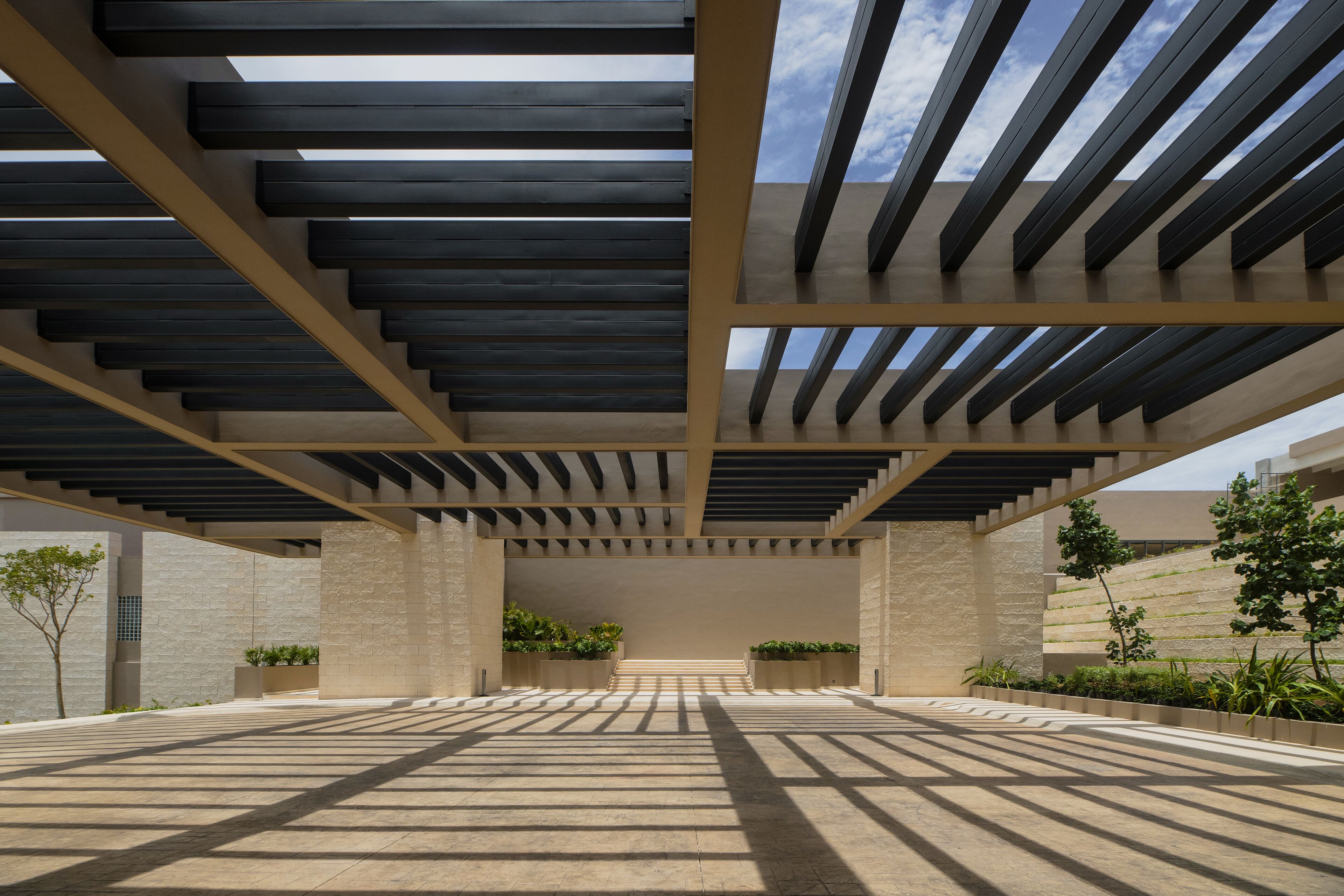 A spacious outdoor area with a modern architectural design, featuring a series of steps leading to a covered area with a view of the sky.