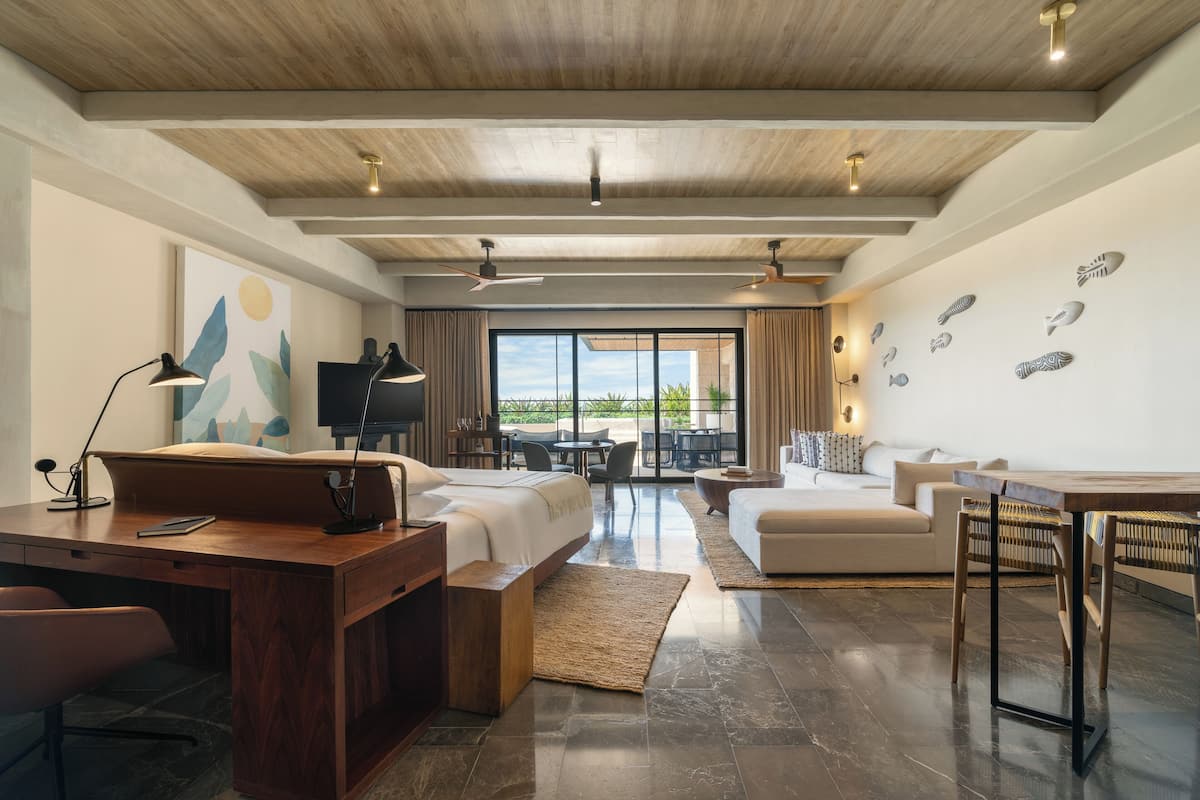 A modern hotel room with a wooden ceiling, a large bed, a desk, and a dining area.