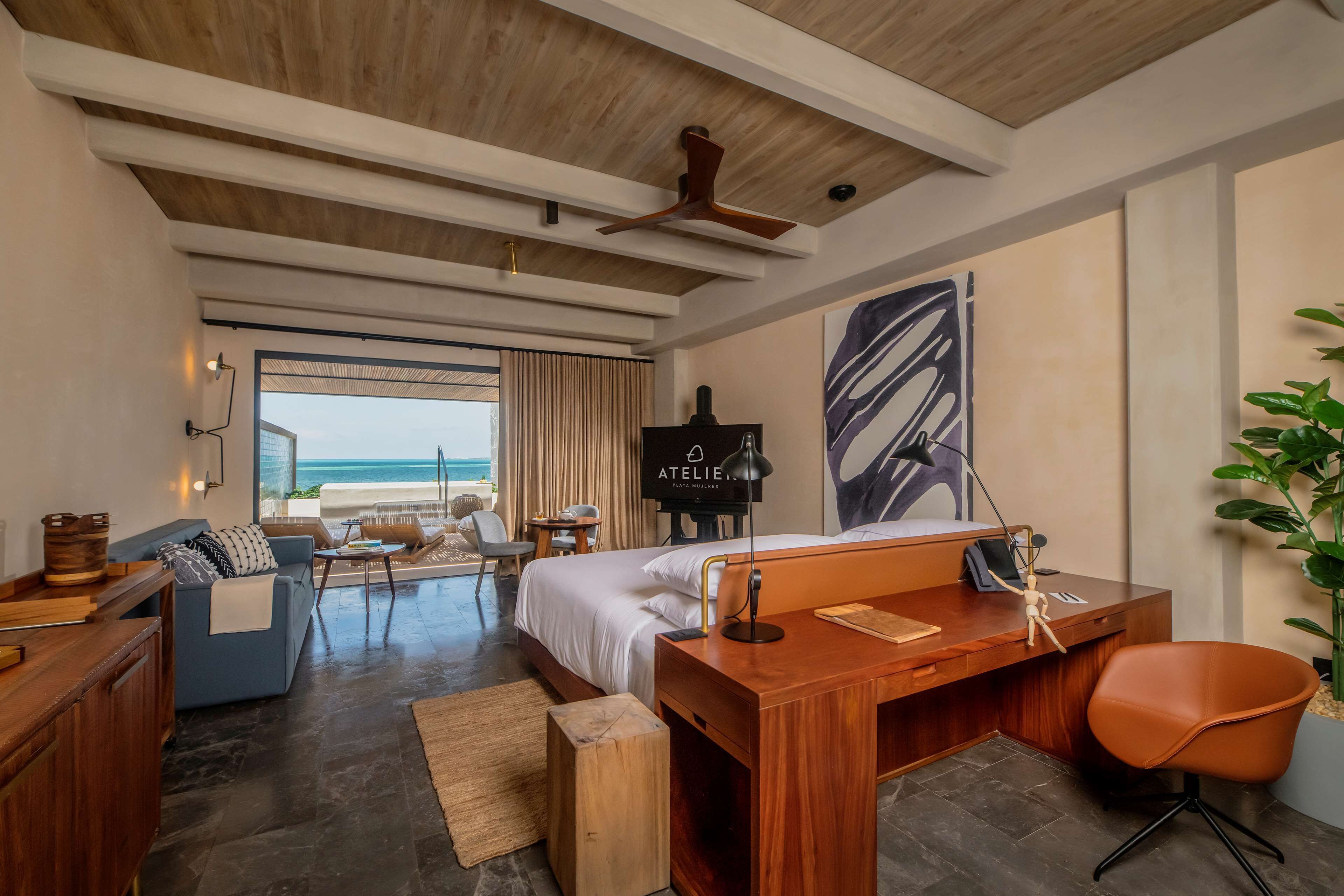 Een moderne hotelkamer met een bed, bureau en zithoek. Het heeft een groot raam met uitzicht op de oceaan.