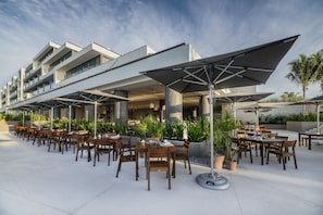 Un área de comedor al aire libre con varias mesas y sillas, sombrillas y plantas en macetas.