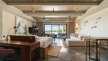 Habitación de hotel moderna con techo de madera, una cama grande, un escritorio con una silla, un sofá, una mesa de comedor con sillas y vistas al exterior a través de amplias ventanas.