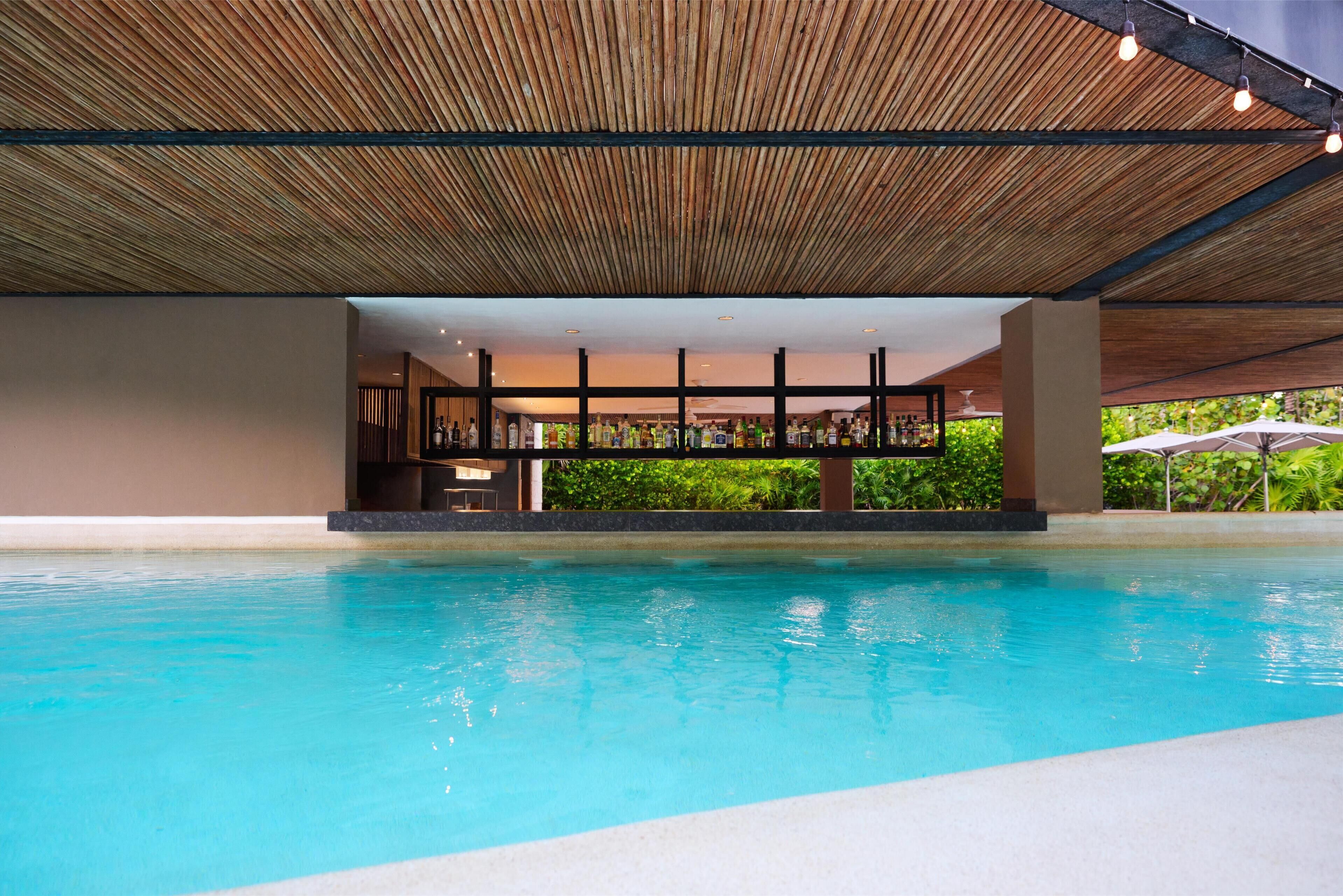 A swimming pool with a wooden ceiling and a bar area with bottles.