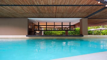 Piscina con techo de madera y zona de bar con botellas.