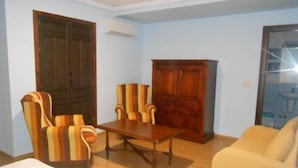 Una habitación con una mesa de madera, dos sillones a rayas, un sofá y un armario.