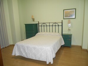 Une chambre à coucher comprenant un lit, une table de chevet, une commode et une lampe fixée au mur.