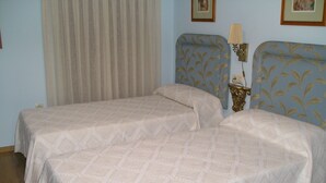 Una habitación con dos camas, una mesita de noche con lámpara y una ventana con cortinas.