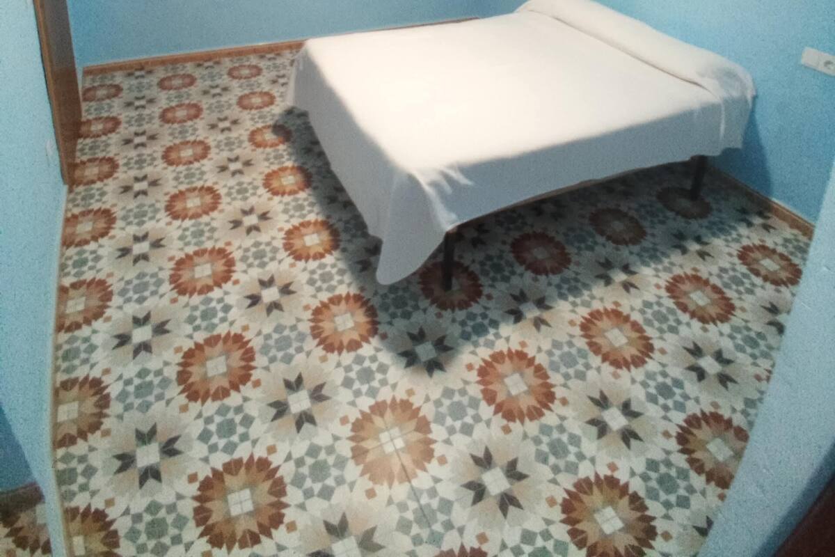 Una habitación pequeña con cama individual, paredes azules y baldosas de suelo estampadas.