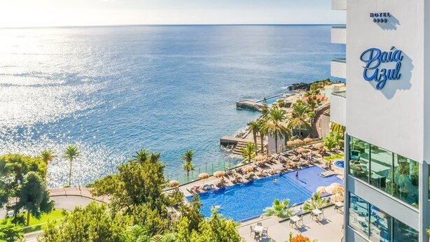 Un hôtel doté d’une piscine donnant sur la mer, bordé de palmiers et offrant une vue sur un ciel dégagé.