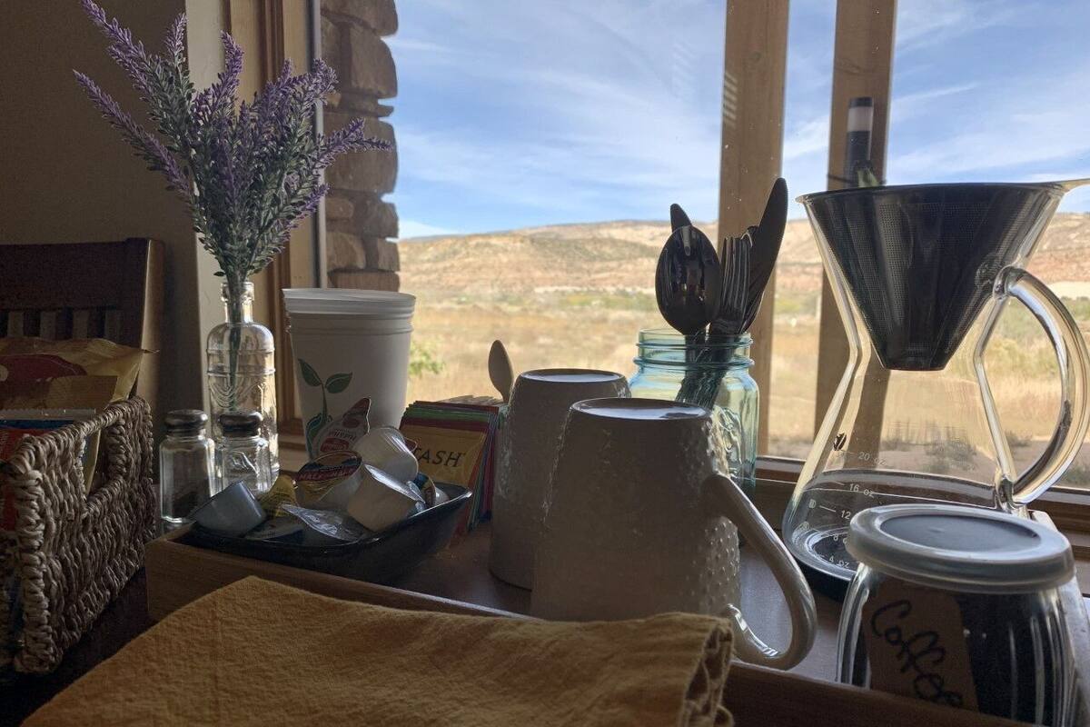 A kitchen counter with a coffee maker, a tea kettle, and a window with a view of a desert landscape.
