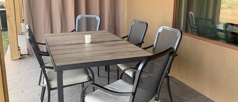 Un porche techado con una mesa de madera y seis sillas, una ventana con vistas y una pared color beige.
