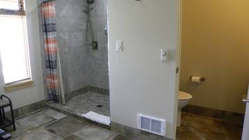 Un baño con ducha, inodoro y ventana con persianas.