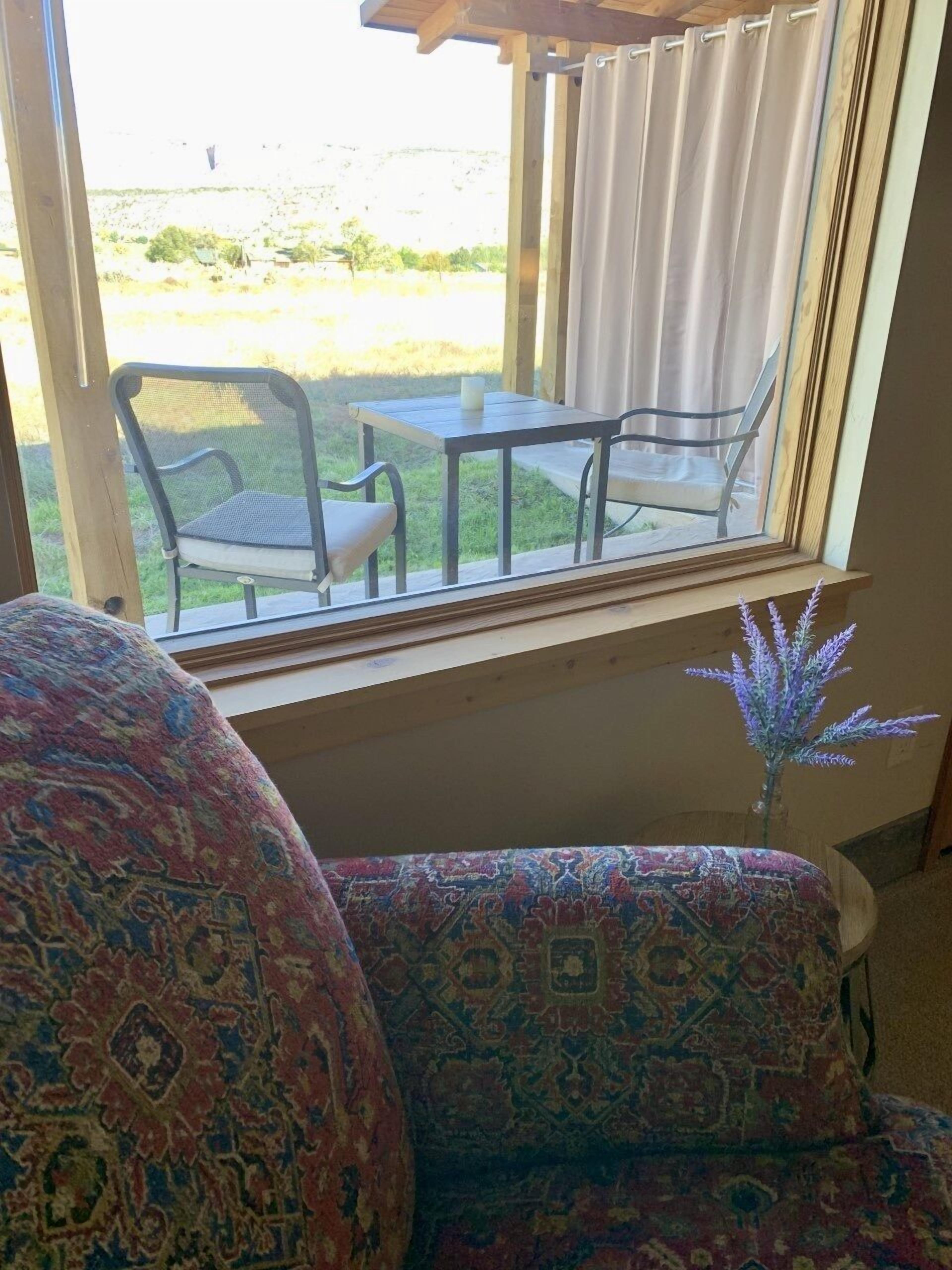 A room with a view of a grassy area and a table with chairs outside a window.