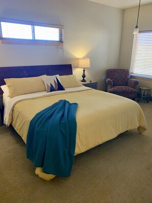 A neatly made bed with a blue throw blanket, a lamp on a bedside table, and a chair in a corner. - Entrada Escalante Lodge (Escalante)