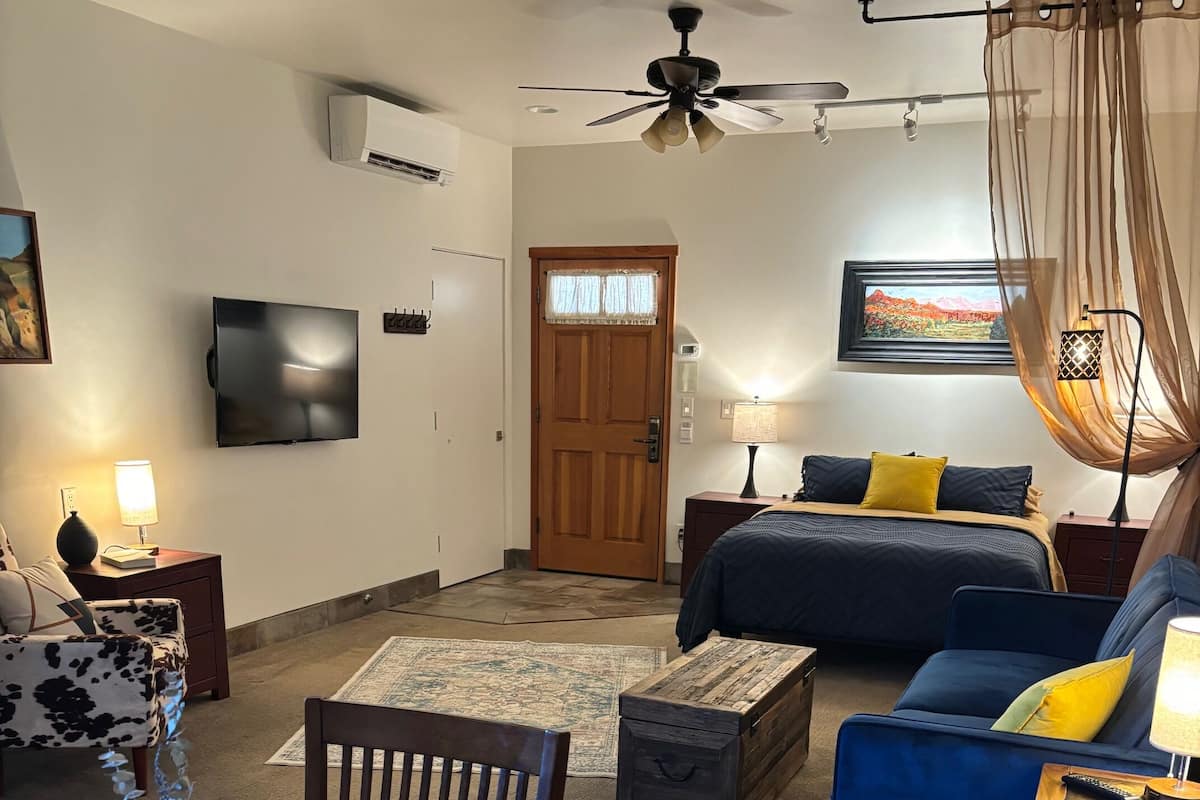 A living room with a wooden dining table, a sofa, a blue armchair, and a ceiling fan.