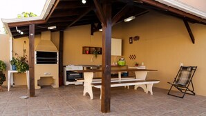 Area patio esterna con tavolo e panche in legno, un barbecue e una sedia pieghevole.