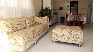 Un soggiorno con divano e poggiapiedi, un tavolo da pranzo con sedie, un angolo cottura e una pianta in vaso.