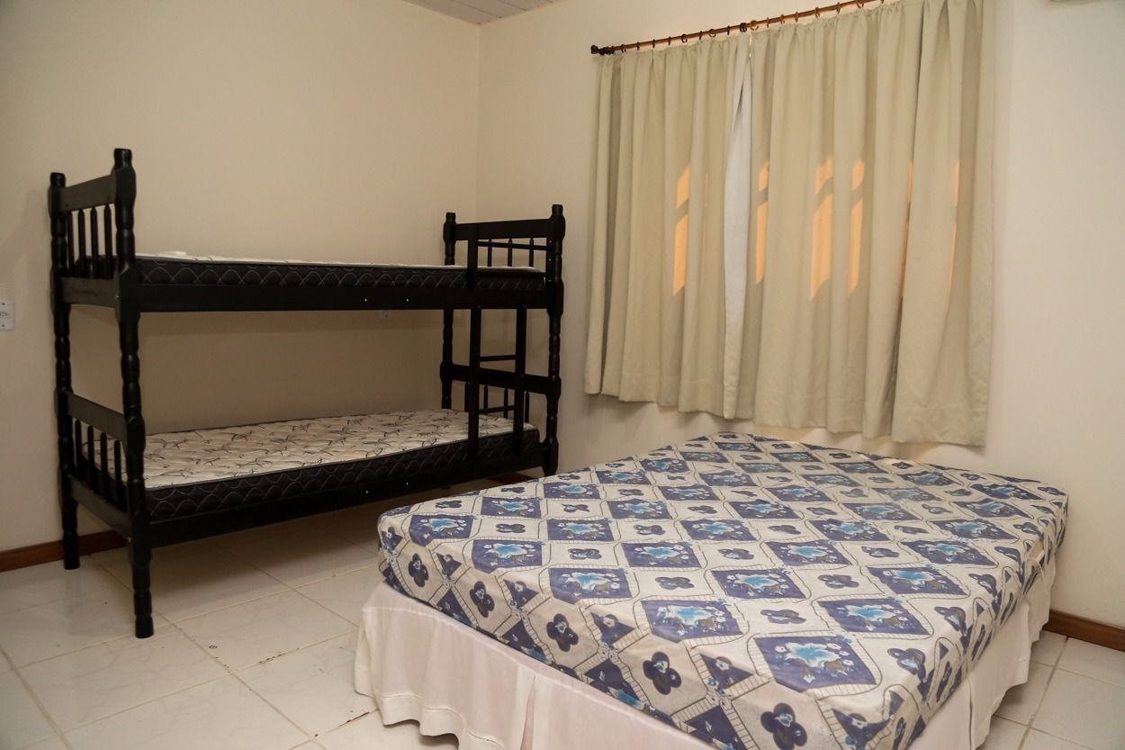 A room with bunk beds and a single bed, a window with curtains, and a tiled floor.