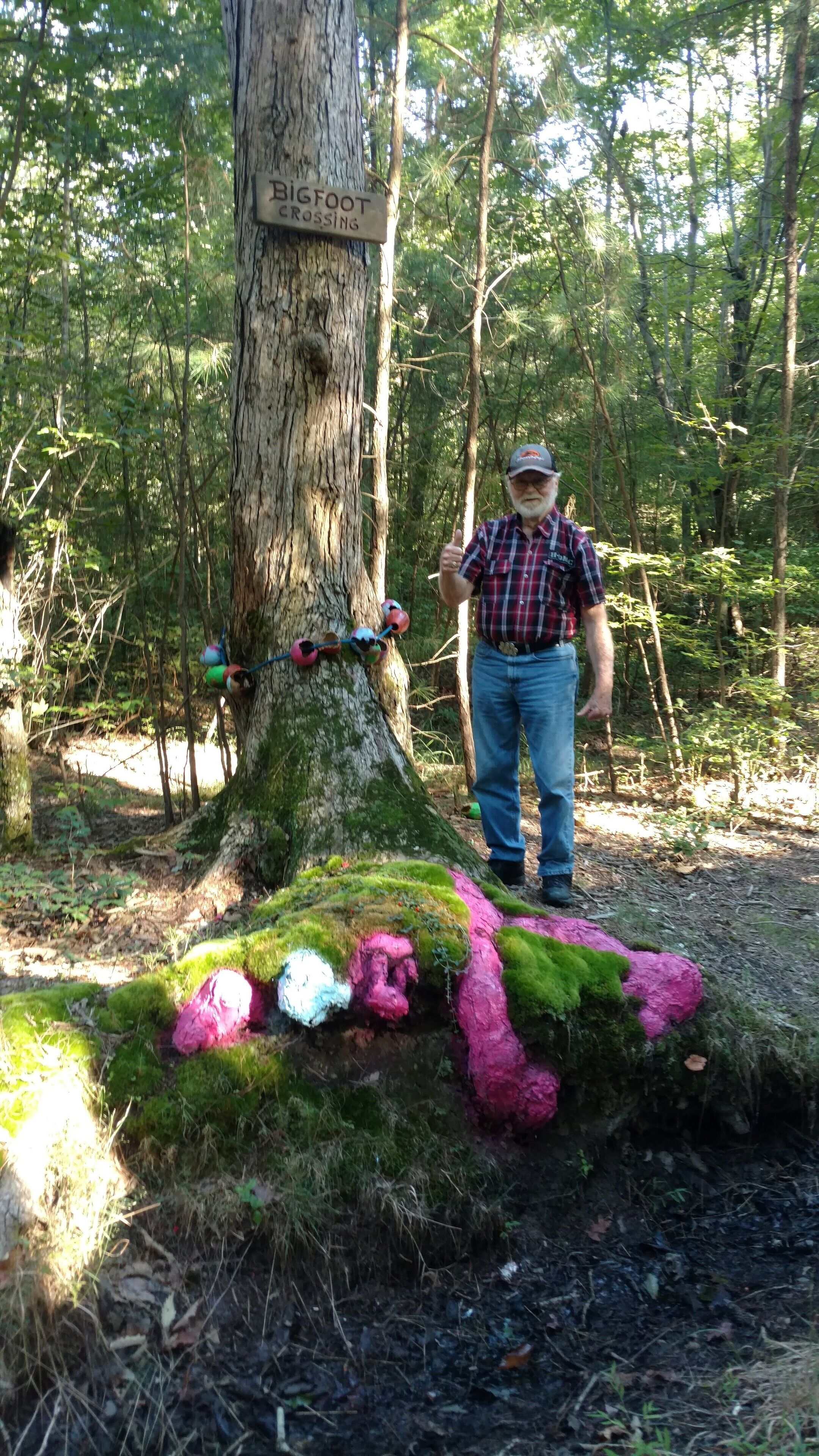 Een man staat naast een boom met een bord waarop staat: BIGFOOT CROSSING.