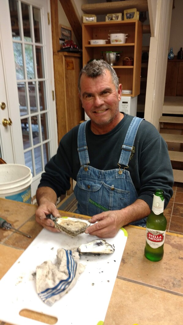 A man in a kitchen preparing food, with a bottle of Stella Artois beer and a cutting board on the counter.