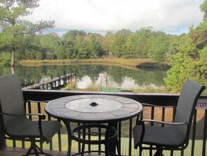 A deck with a round table and four chairs, overlooking a calm lake and dense forest.