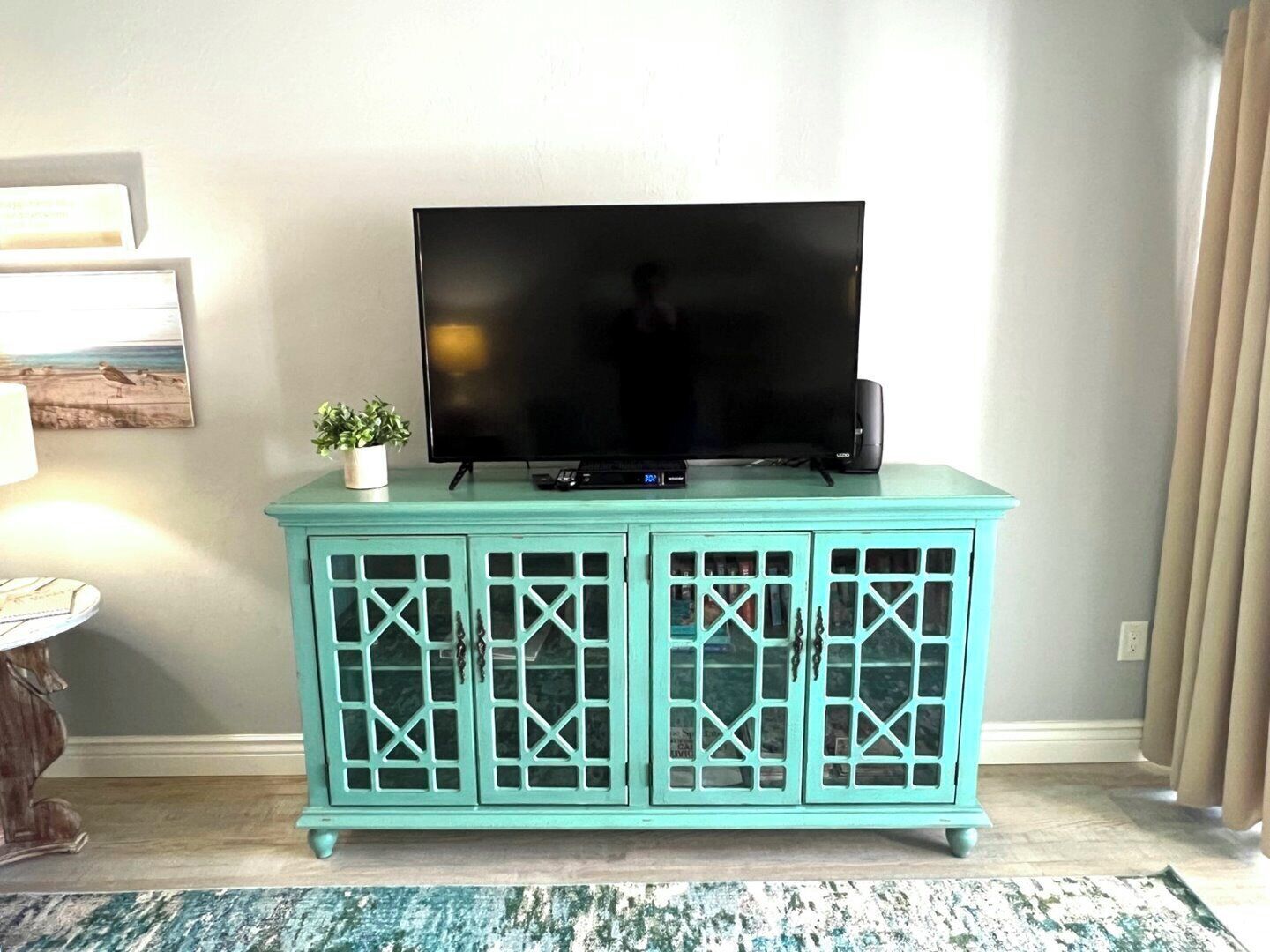 Een smaragdgroene kast met een flatscreen televisie erboven, een klein plantje en een decoratief object aan de linkerkant.
