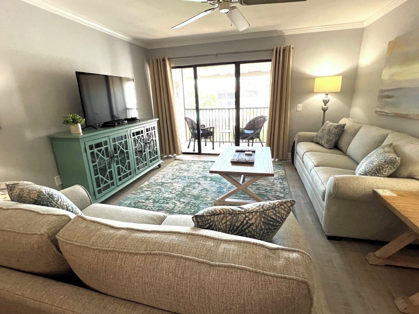 Un salón con sofá, mesa de centro, televisor en un mueble bajo y un balcón con sillas.