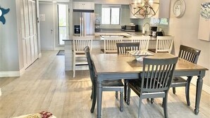 Eine moderne Küche mit weißen Schränken, einer zentralen Kochinsel und einem Essbereich mit einem dunklen Holztisch und Stühlen.