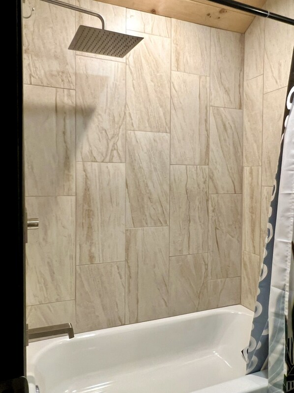 A bathroom with a bathtub, a showerhead, and tiled walls.