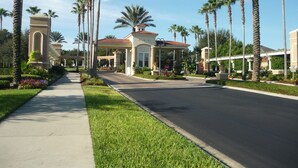 A gated entrance with palm trees, a clear sky, and a well-maintained lawn. - 4 BR Pool Home/Close to Disney/Universal/Pool/Spa/BBQ/Wifi/Guard Gated Resort (Kissimmee)