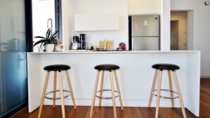 Una cocina moderna con encimera blanca, tres taburetes de madera y electrodomésticos de acero inoxidable.