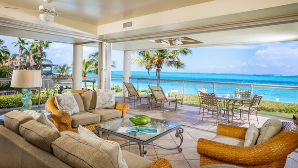 A spacious outdoor seating area with a view of the ocean, furnished with wicker chairs and a glass-top table. - Relax in your very own private paradise (Providenciales)