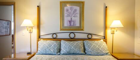 A neatly made bed with patterned bedding, two bedside lamps, and a framed artwork on the wall.