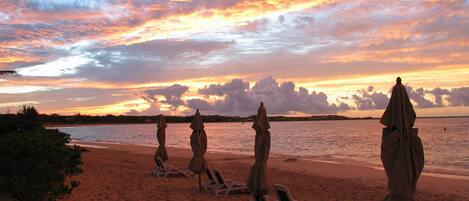 A beach with lounge chairs and umbrellas, a calm sea, and a sunset sky.