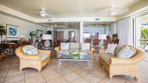 A spacious living area with wicker furniture, a glass coffee table, and a view into the kitchen. - Relax in your very own private paradise (Providenciales)