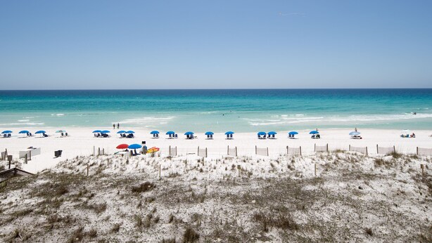 A beach with white sand, clear blue water, and several umbrellas.
