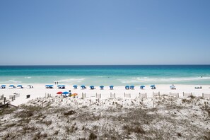 Een strand met wit zand, helderblauw water en meerdere parasols.
