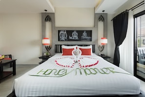 Hotelkamer met een bed, versierd met een zwaan en 'honeymoon'-decoratie, een nachtkastje met lamp, een kunstwerk aan de muur en een raam met gordijnen.