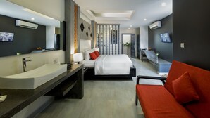 A modern hotel room with a large bathtub, a bed with red pillows, a sofa, and a TV on the wall. - Central Residence Suite  (Krong Siem Reap)