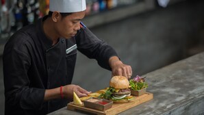 A chef preparing a burger with fries and condiments on a wooden board. - Central Residence Suite  (Krong Siem Reap)