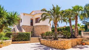 Eine mediterran gestaltete Villa mit Steinaußenwand, gebogenem Eingang und einer Steintreppe zum Eingang.