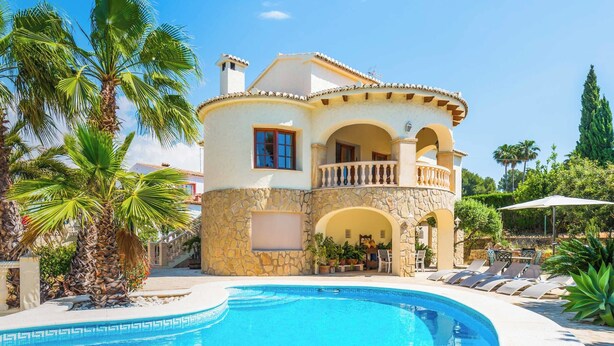 Ein zweistöckiges Haus mit Pool, Steinmauern und einem Balkon.