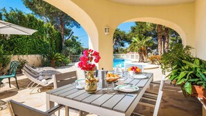 Eine sonnige Terrasse mit Frühstückstisch, umgeben von Bögen und Grünpflanzen.